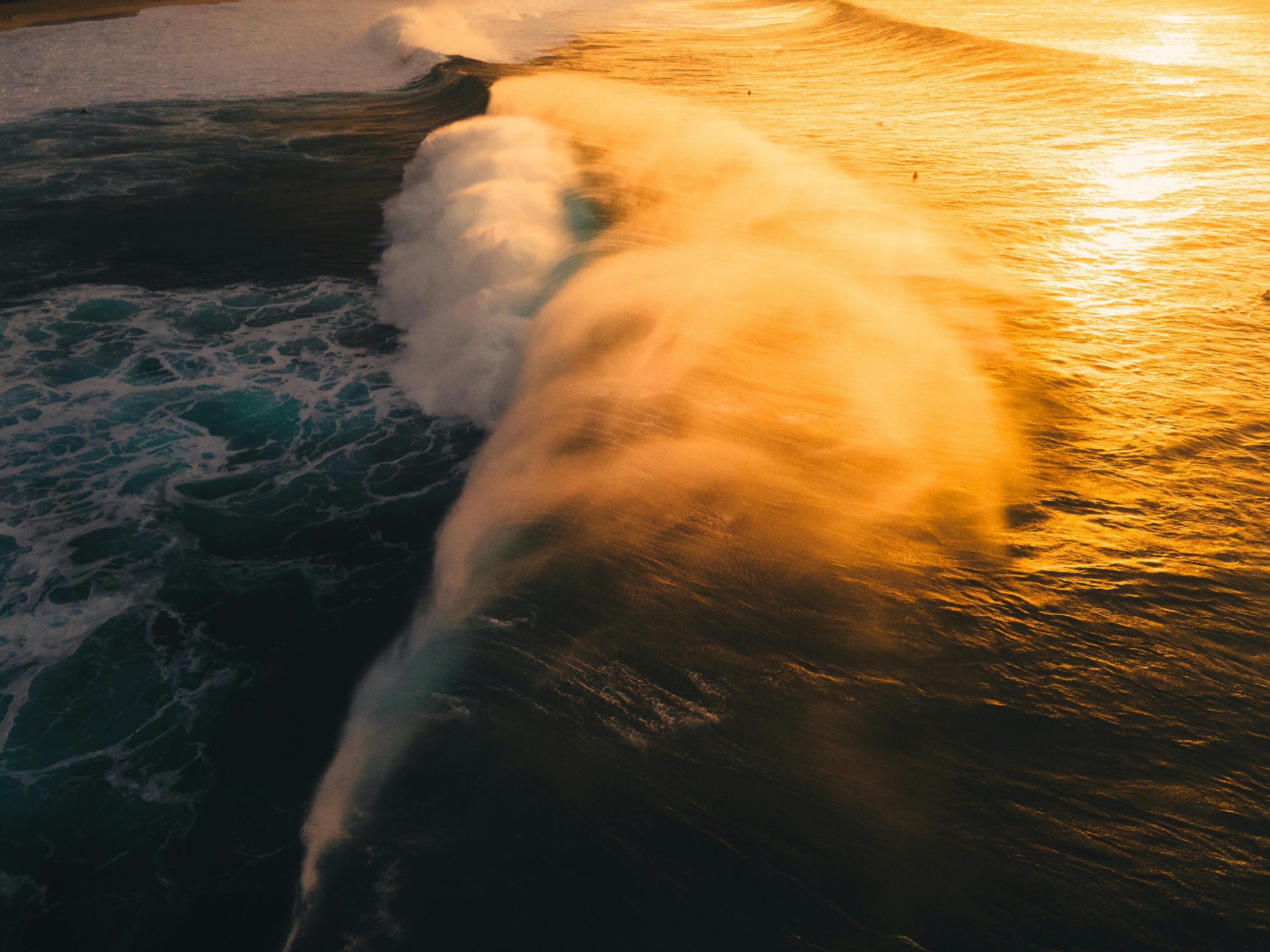 Aerial view of powerful ocean waves crashing under a stunning sunset in Hawaii.