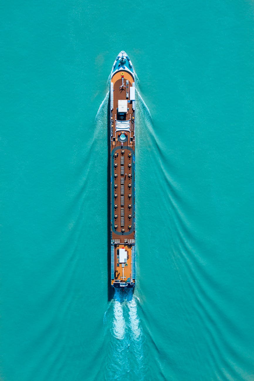 Drone shot of a cruise ship navigating turquoise waters, creating ripples and waves.