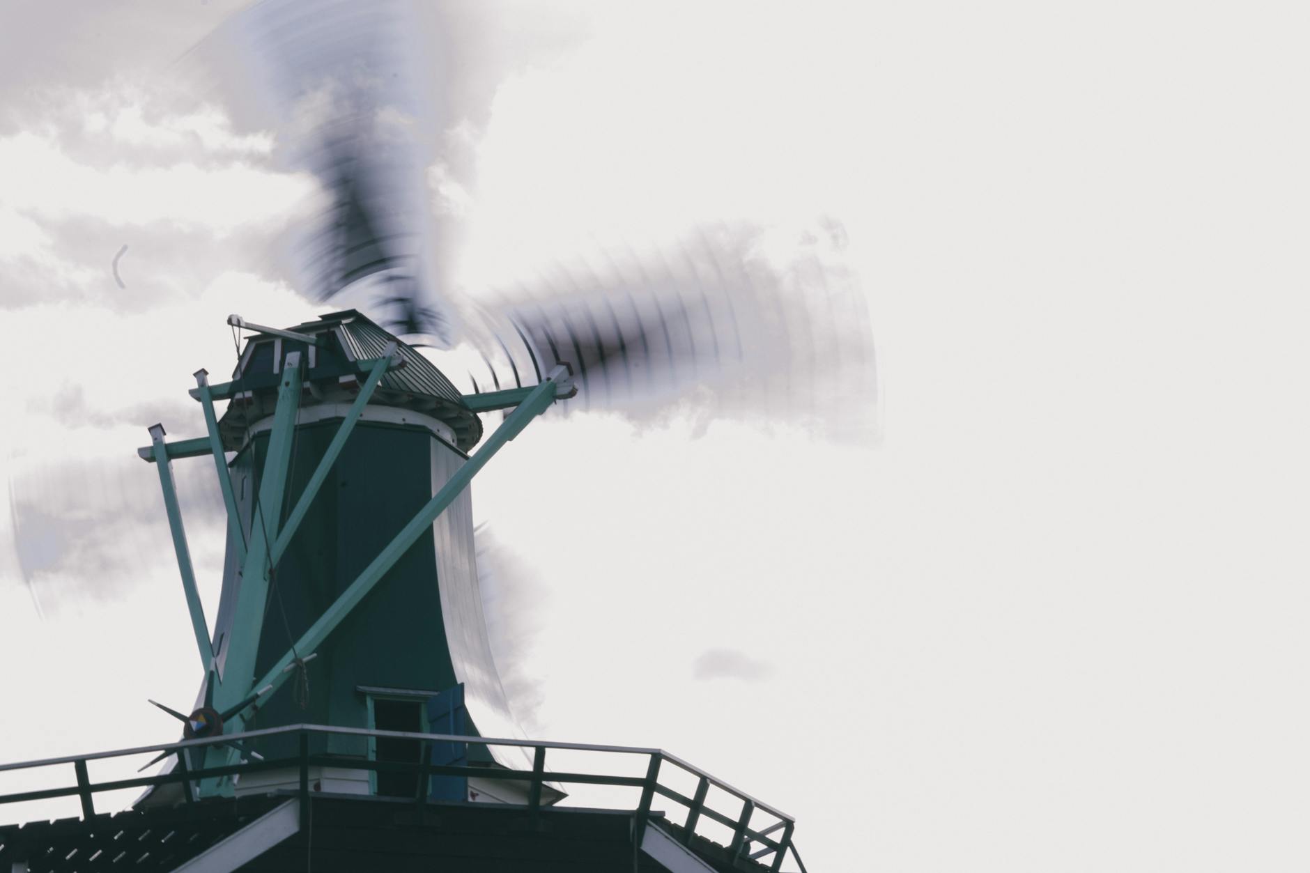 Windmill in motion with blurred blades set against a backdrop of a cloudy sky, symbolizing renewable energy.